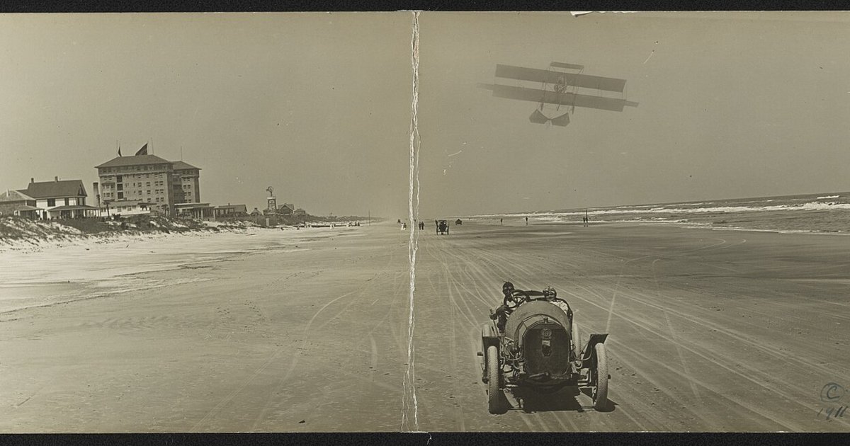 Historic photo of cars racing on the sand at Daytona Beach with a biplane overhead
