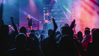 A joyful concert crowd with hands in the air under colorful stage lights