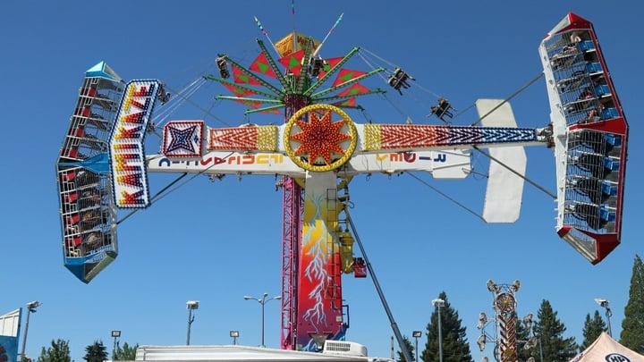 A colorful spinning carnival ride against a bright blue sky at a fair