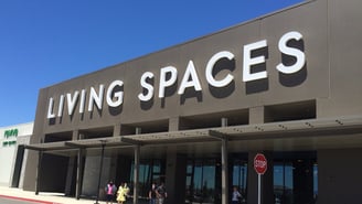 The front of a Living Spaces furniture store with large white letters on a gray facade under a blue sky, in Manteca, California