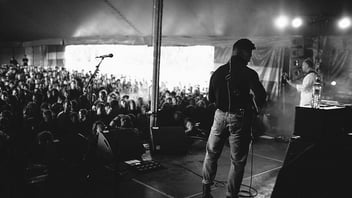 A duo performs on a covered stage in front of a packed crowd