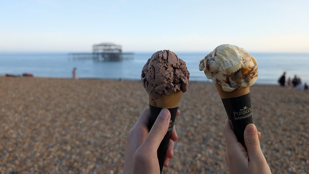 Two ice cream cones held up against the sea on a sunny beach