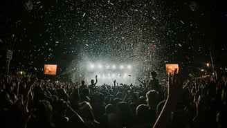 A lively outdoor music festival crowd under string lights and daytime sky