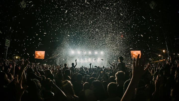 A lively outdoor music festival crowd under string lights and daytime sky