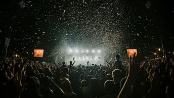 A lively outdoor music festival crowd under string lights and daytime sky